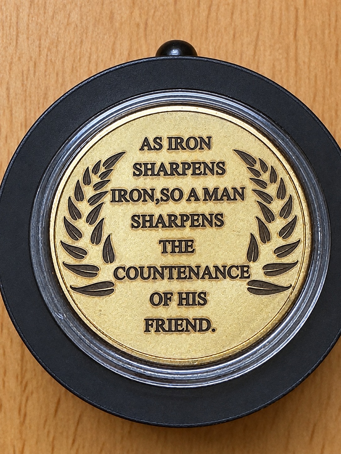 Brass challenge coin engraved with an iron sharpens iron scripture quotation