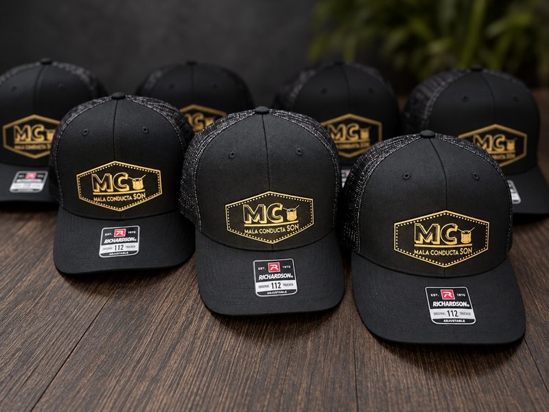 Black trucker hats with custom gold engraved Mala Conducta Son patches