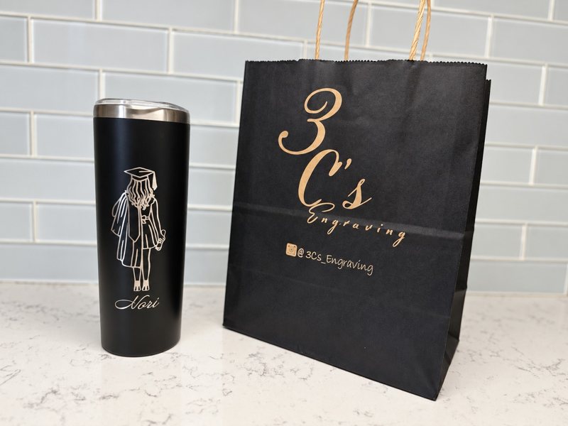 Black graduation tumbler engraved Nori beside a 3Cs Engraving gift bag